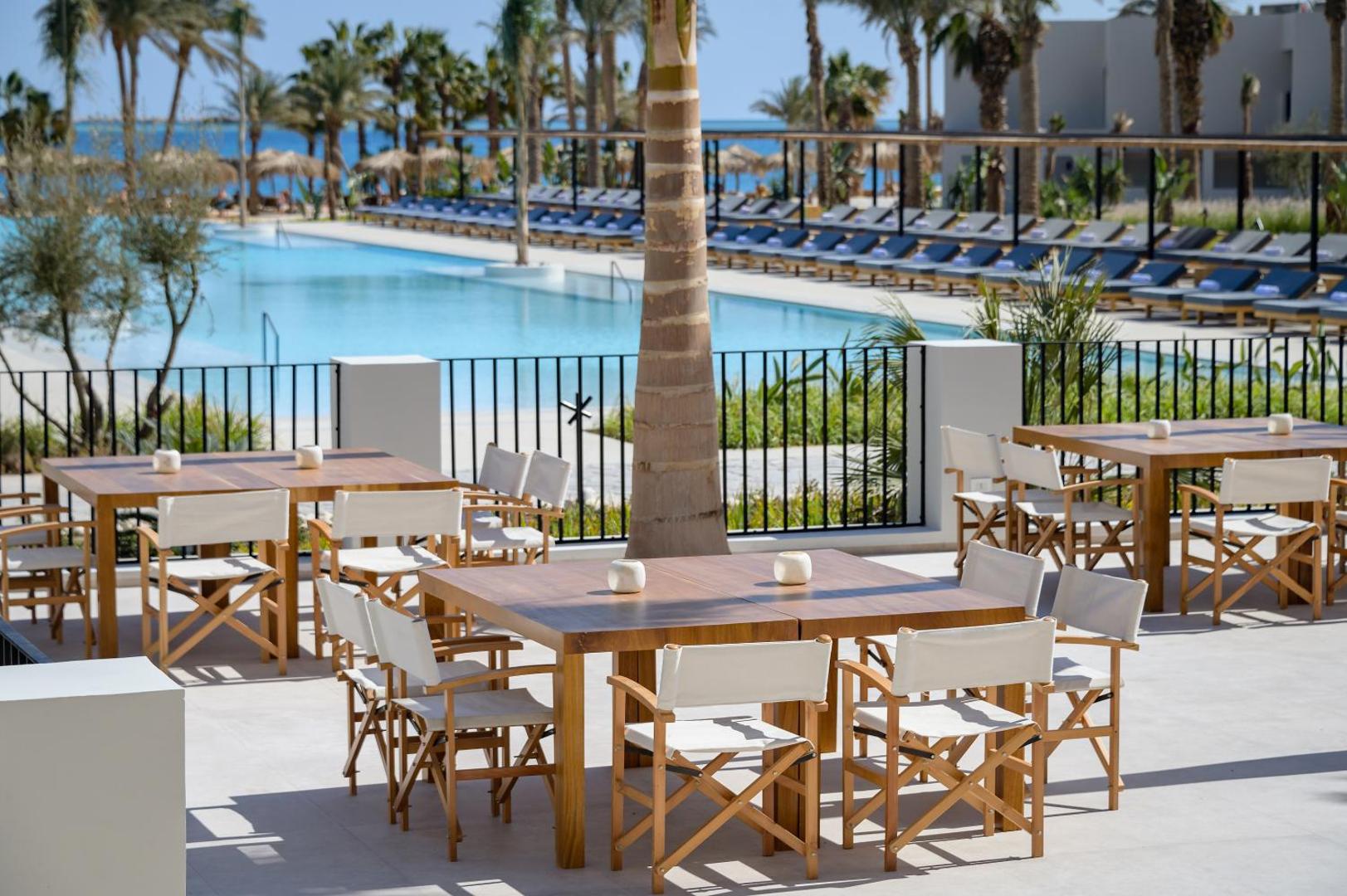 Serry Beach Resort āra terase ar koka galdiem pie baseina un skatu uz Sarkano jūru Hurgadā, Ēģiptē.