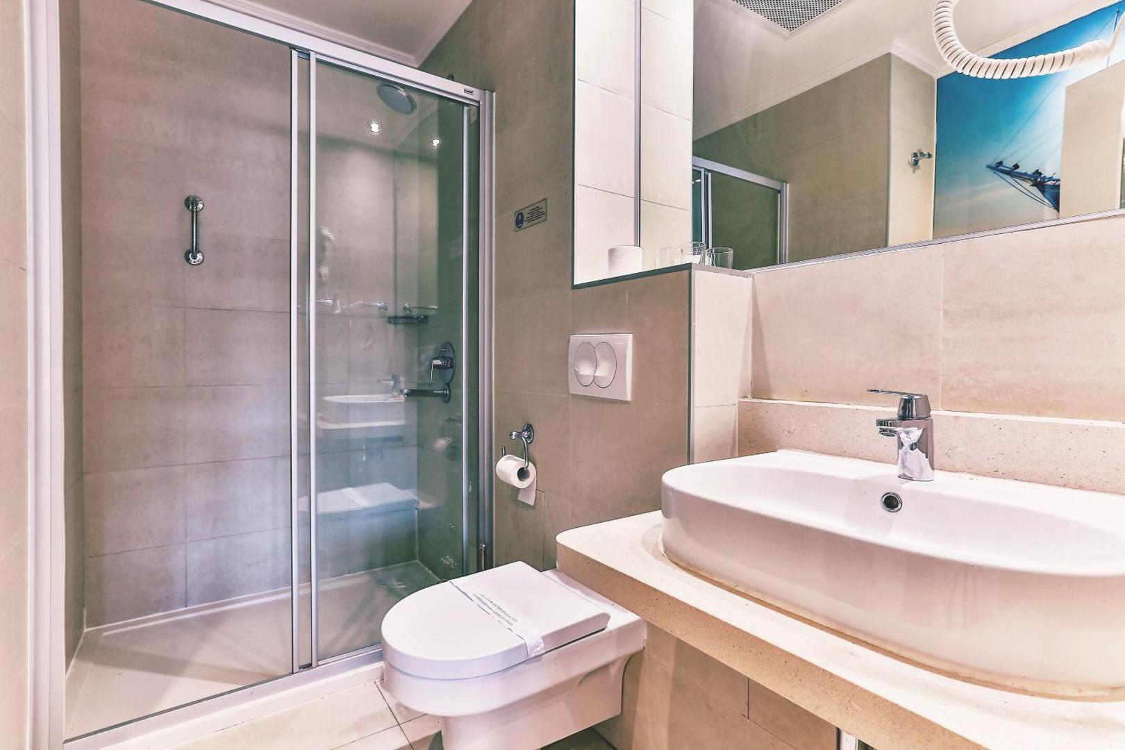 Carine Hotel Delfin numura vannas istaba ar dušas kabīni, izlietni un spoguli — gaiši bēša flīžu apdare un mūsdienīgs dizains
