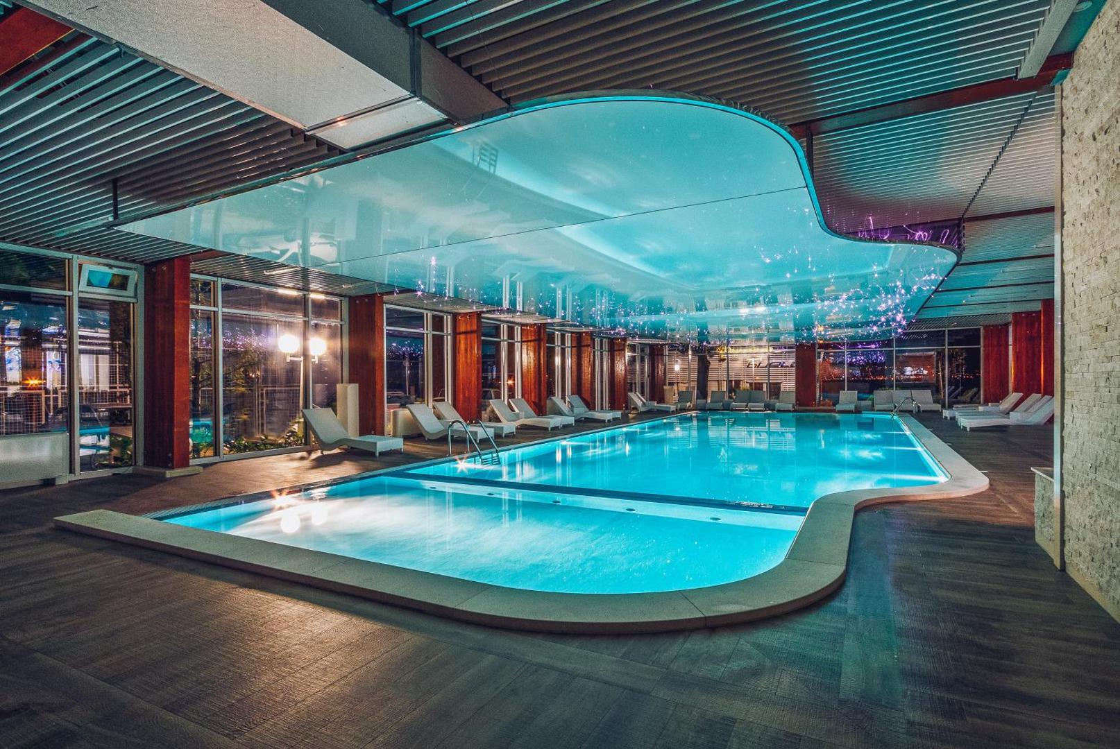 Carine Hotel Delfin iekštelpu baseins ar modernu apgaismojumu un atpūtas krēsliem Bijelā, Melnkalnē — panorāmas logi un dekoratīvi griesti