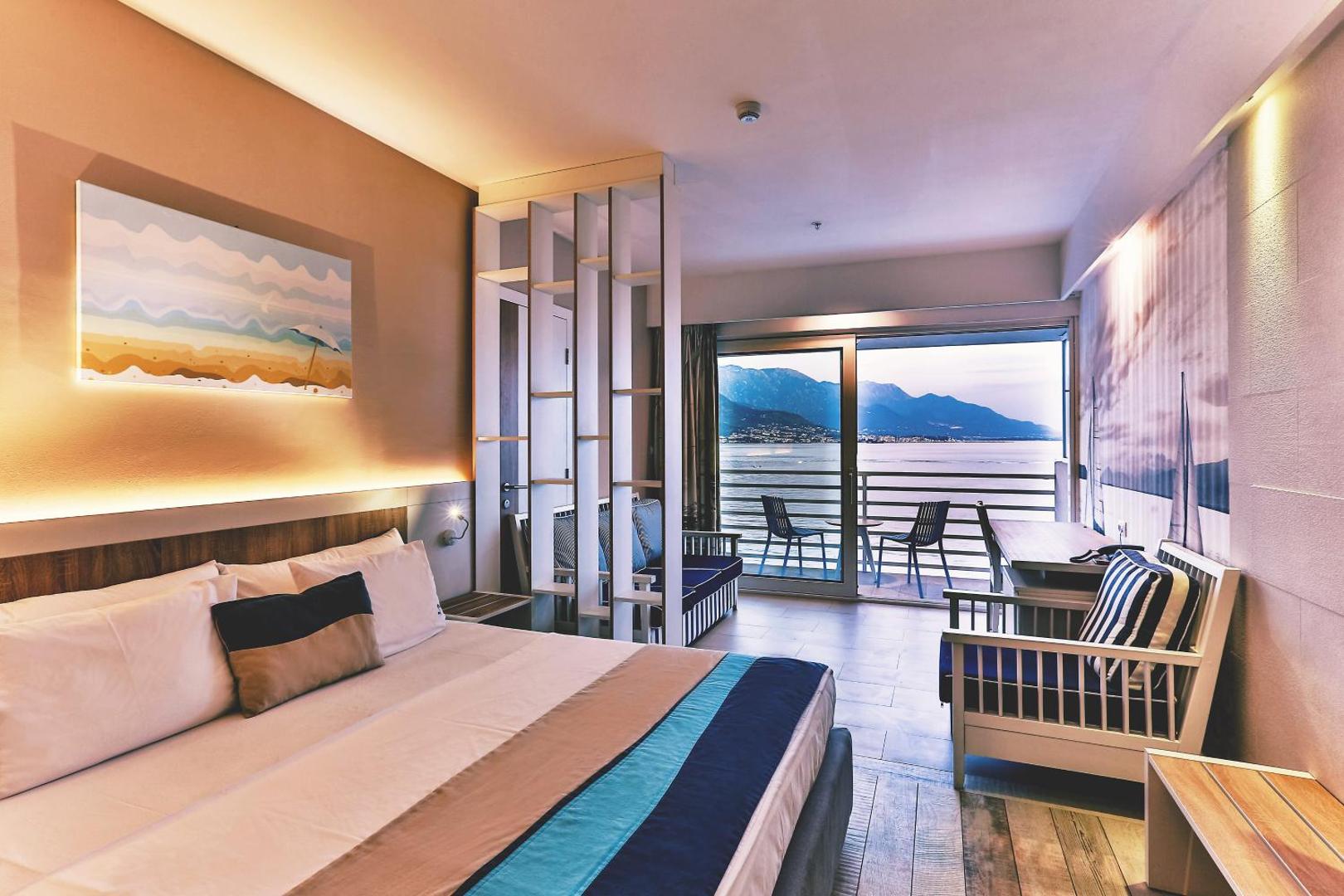 Carine Hotel Delfin moderns viesnīcas numurs ar plašu gultu, atpūtas zonu un stikla durvīm uz balkonu ar skatu uz jūru