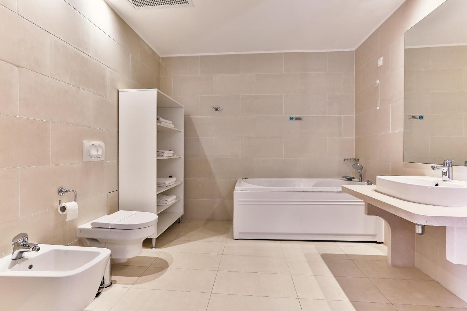 Plaša Carine Hotel Delfin vannas istaba ar vannu, bidē un dvieļu plauktu — gaišs un tīrs interjers viesu ērtībām