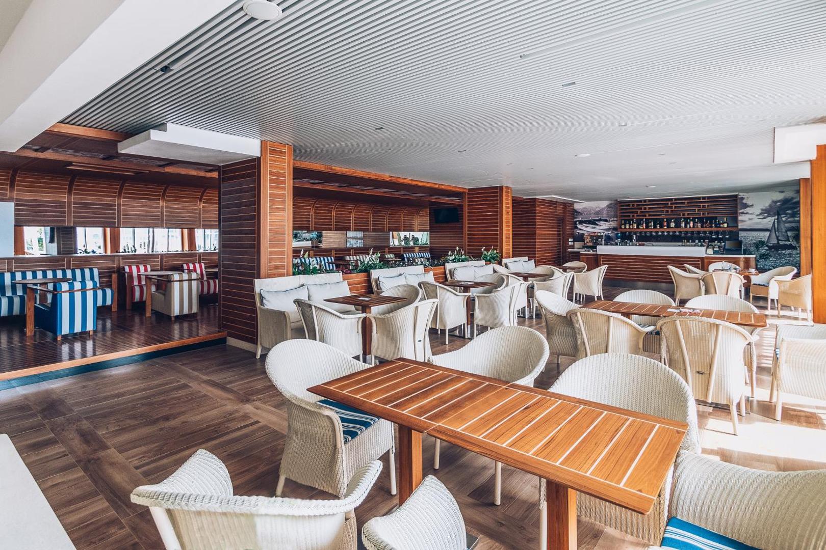 Carine Hotel Delfin mājīgs bārs un atpūtas zona ar koka apdari, pītiem krēsliem un svītrainiem dīvāniem Melnkalnes piekrastē