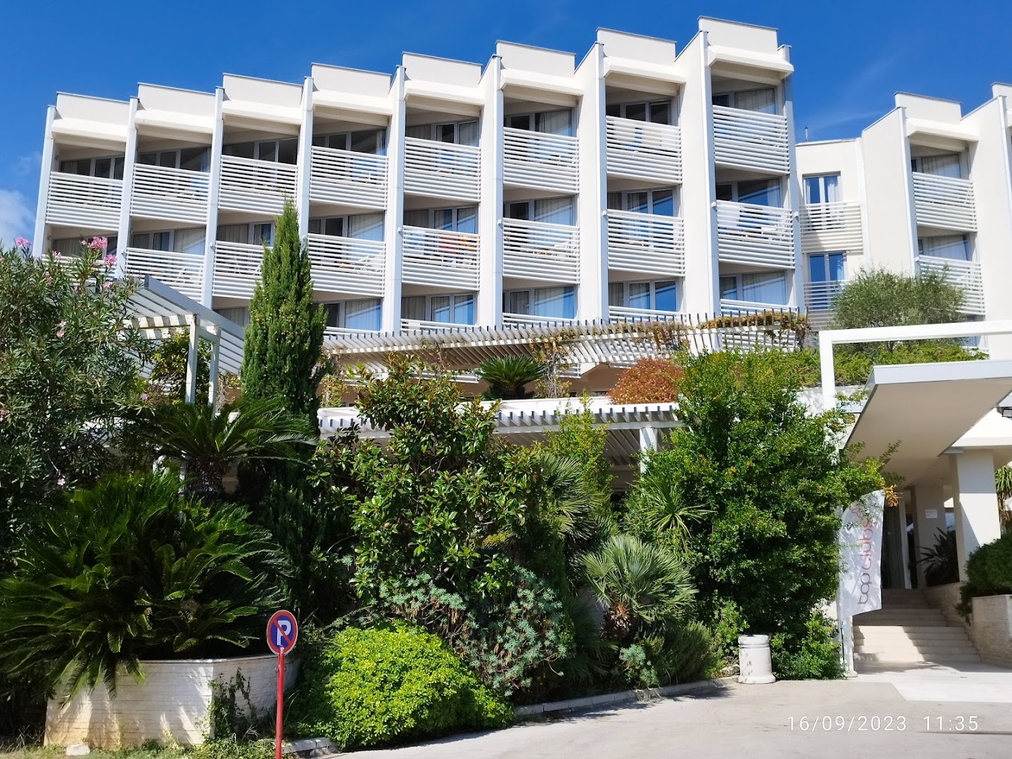 Carine Hotel Delfin numuru balkoni un ieeja, ko ieskauj lekni zaļumi, palmas un dekoratīvie augi saulainā laikā