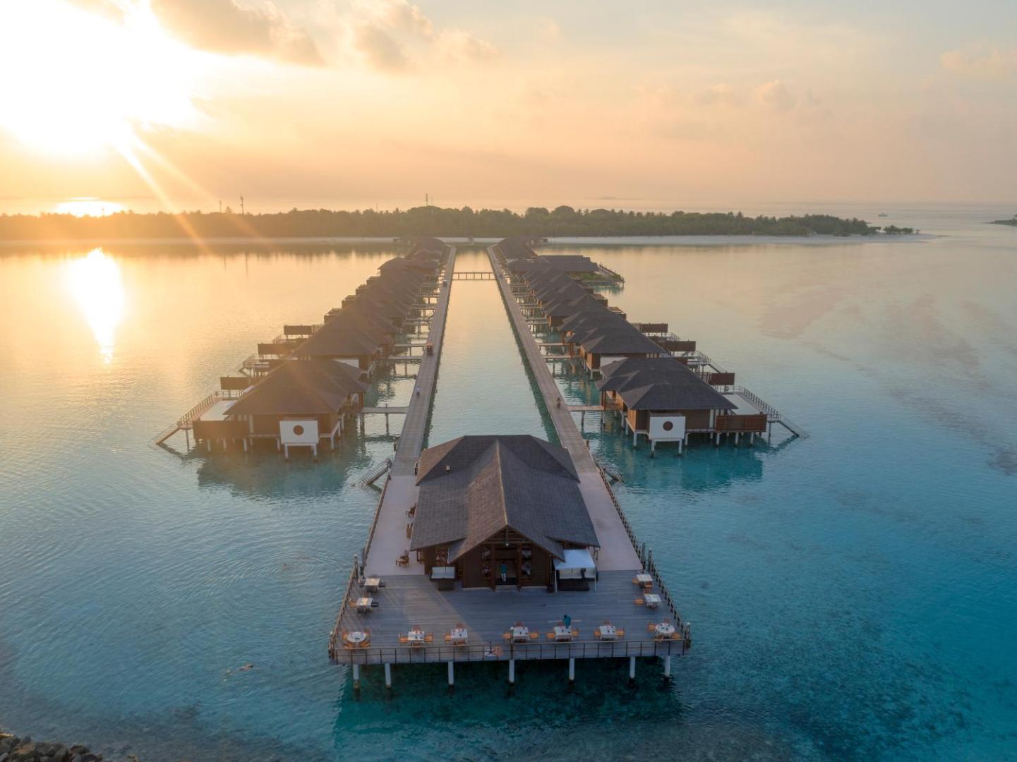 Saulrieta skats uz Villa Nautica Paradise Island ūdens villu rindu un restorānu uz koka laipām Maldīvu salu lagūnā