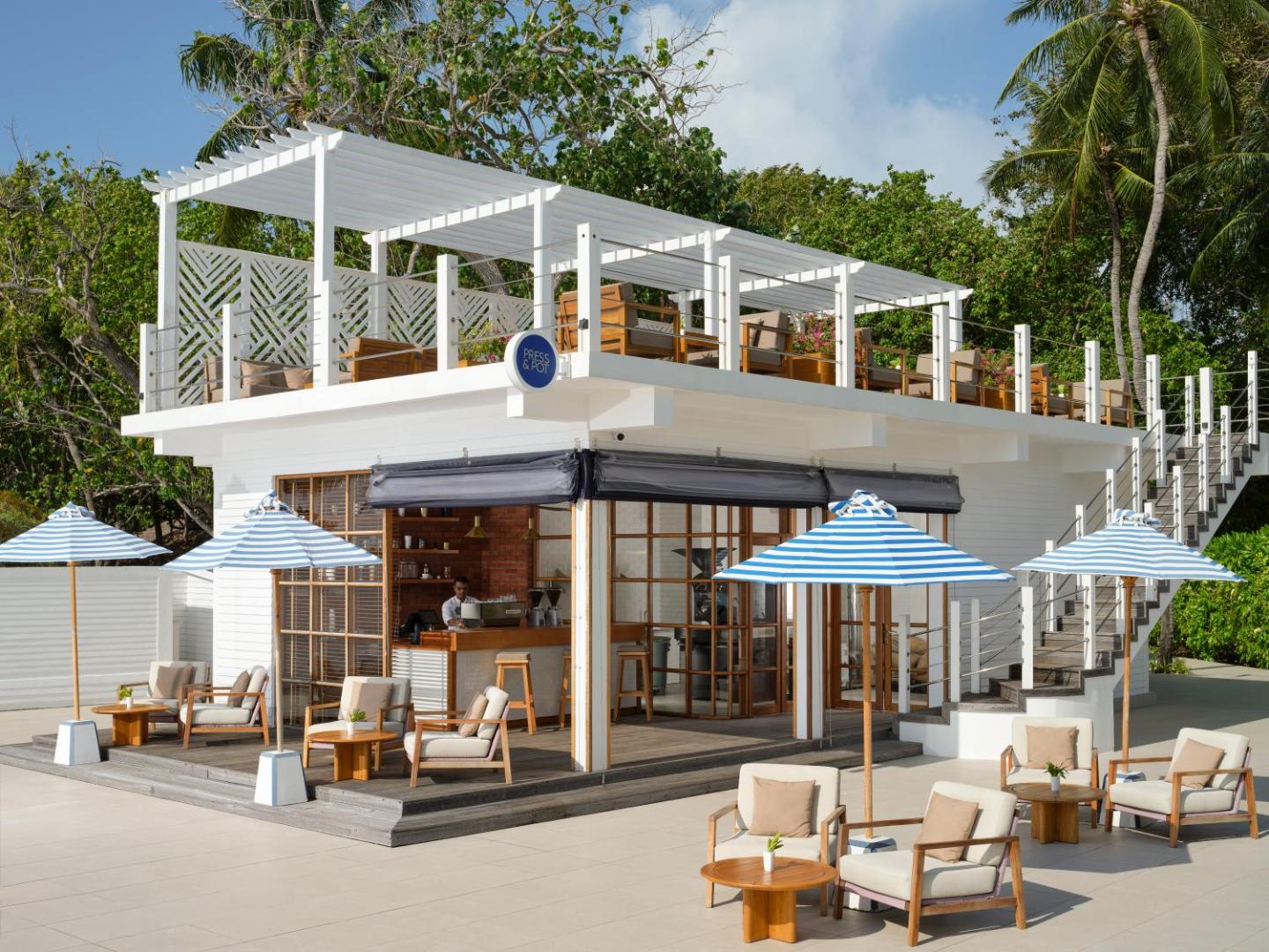 Villa Nautica Paradise Island modernā kafejnīca Press & Pot ar divstāvu terasi, baltu pergolu un saulessargiem