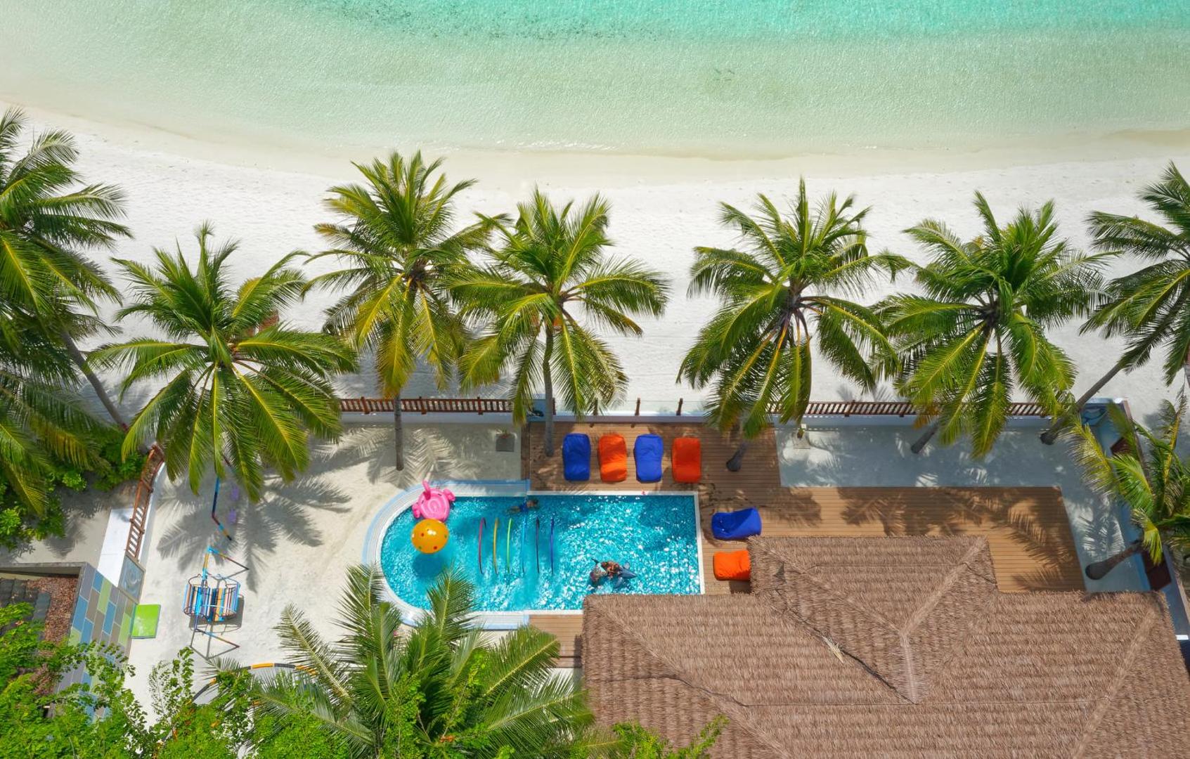 Aerofoto skats uz Villa Nautica Paradise Island bērnu baseinu un balto smilšu pludmali Maldīvu salās starp augstām palmām