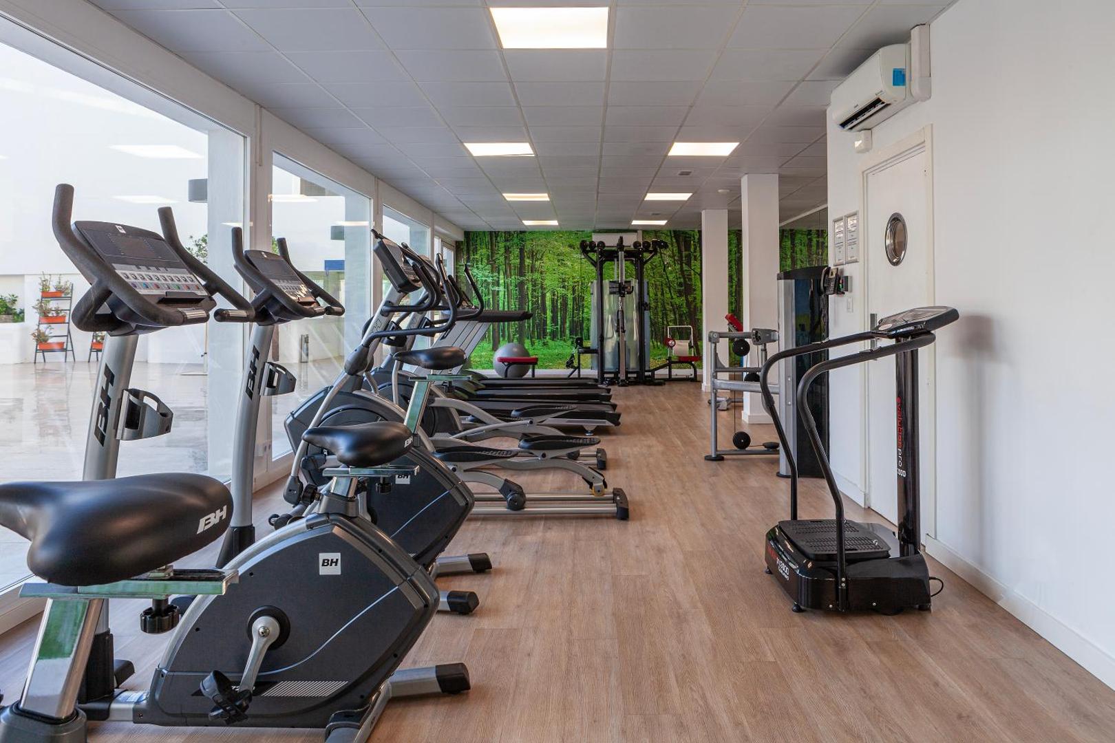 Hotel Alay fitness centrs ar velotrenažieriem, skrejceļiem un lieliem logiem, kas vērsti uz gaišu iekšpagalmu