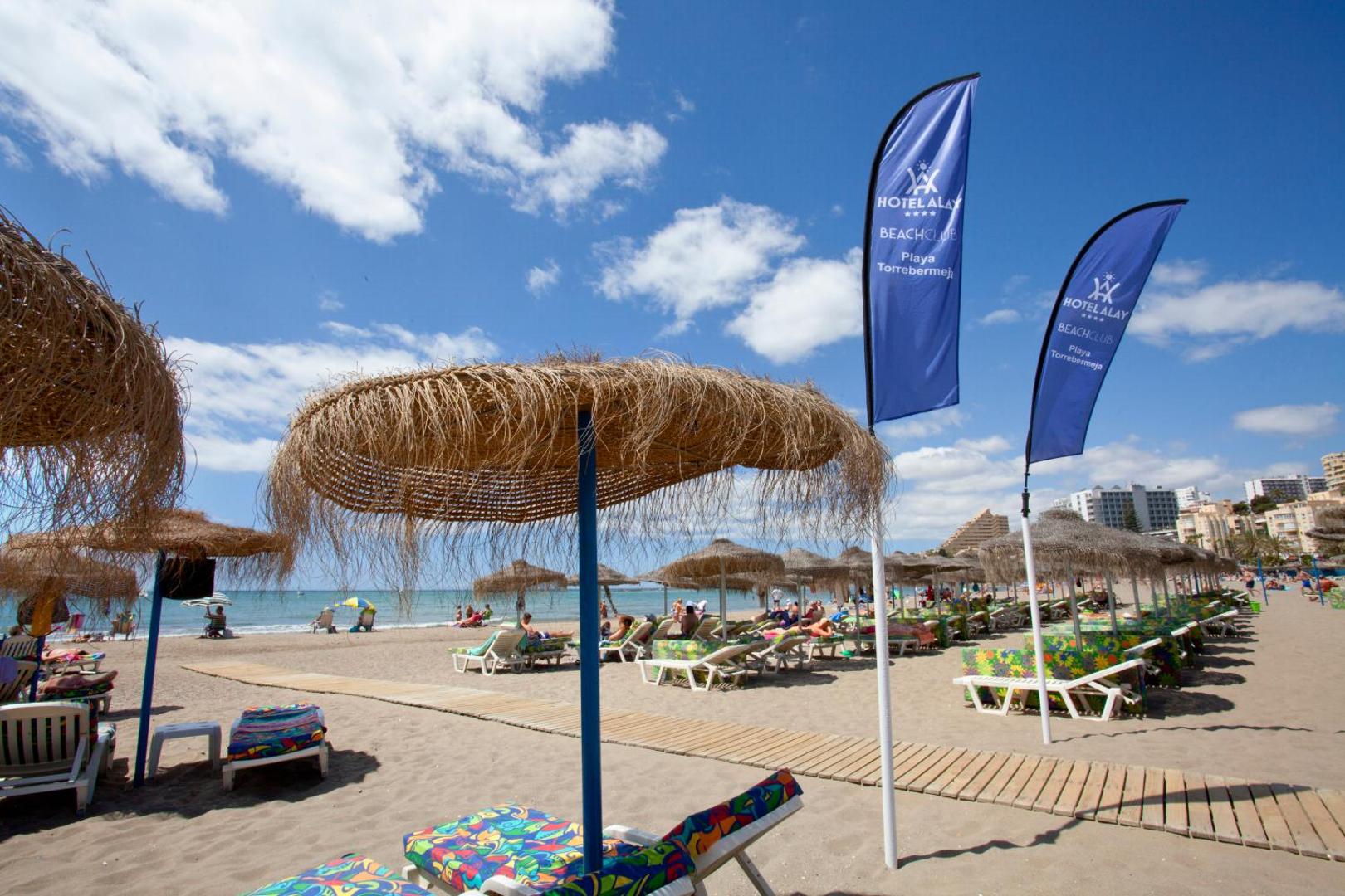 Hotel Alay Beach Club zona ar ziliem karogiem un salmu saulessargiem Benalmadenas piekrastē Kosta del Solā