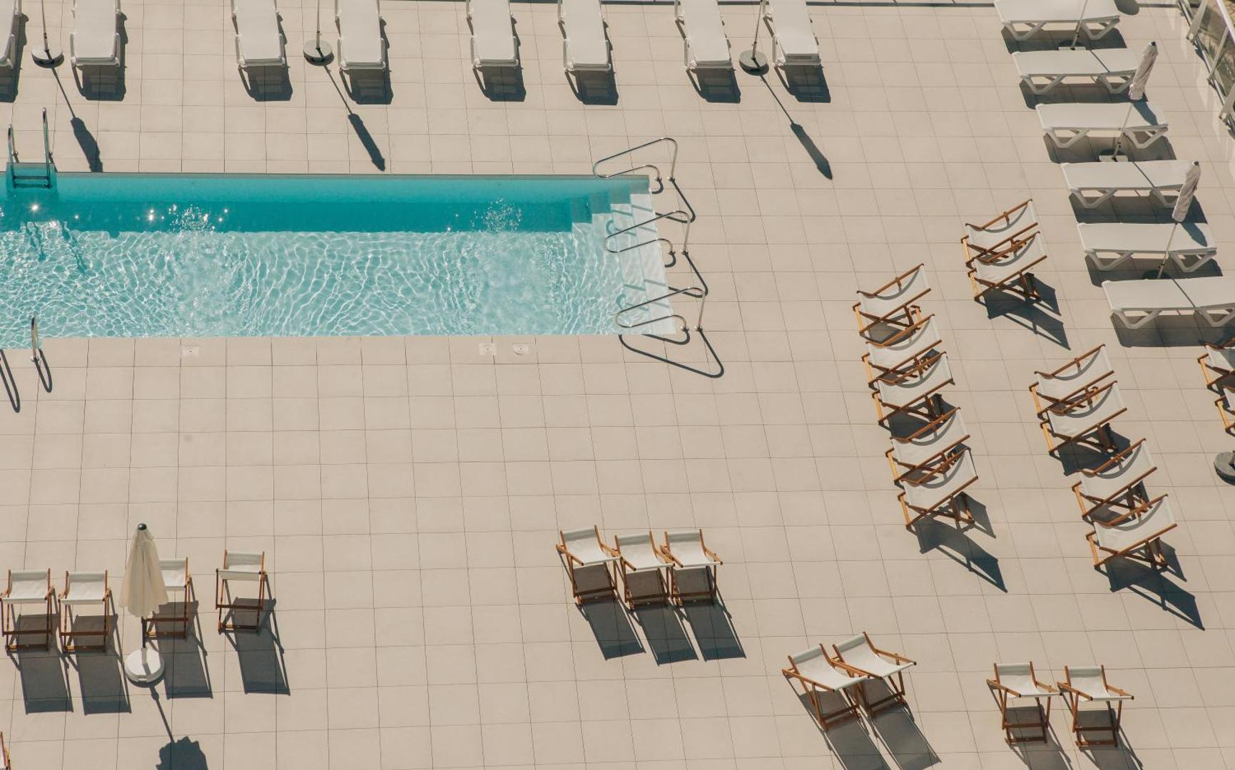 Hotel Alay baseina mala ar dzidru ūdeni un sakārtotiem zviļņiem uz gaišas flīžu terases — moderna un minimālistiska atpūtas vide