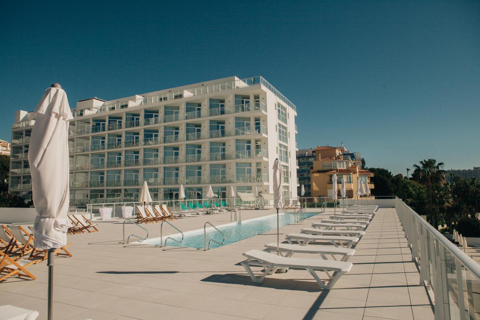 Hotel Alay āra baseins uz terases Benalmadenā — gaiša atpūtas zona ar sauļošanās krēsliem, saulessargiem un skatu uz viesnīcas fasādi