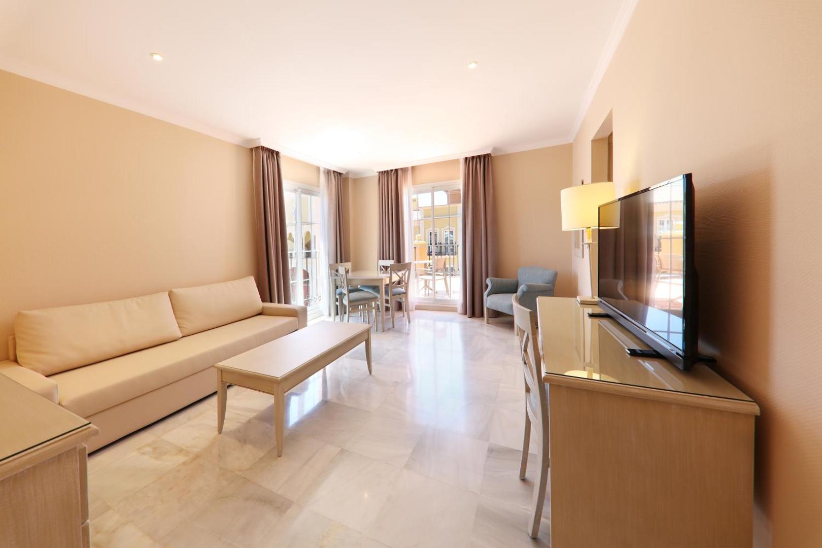 Iberostar Malaga Playa numura viesistabas zona ar dīvānu, galdu, televizoru un marmora grīdu.