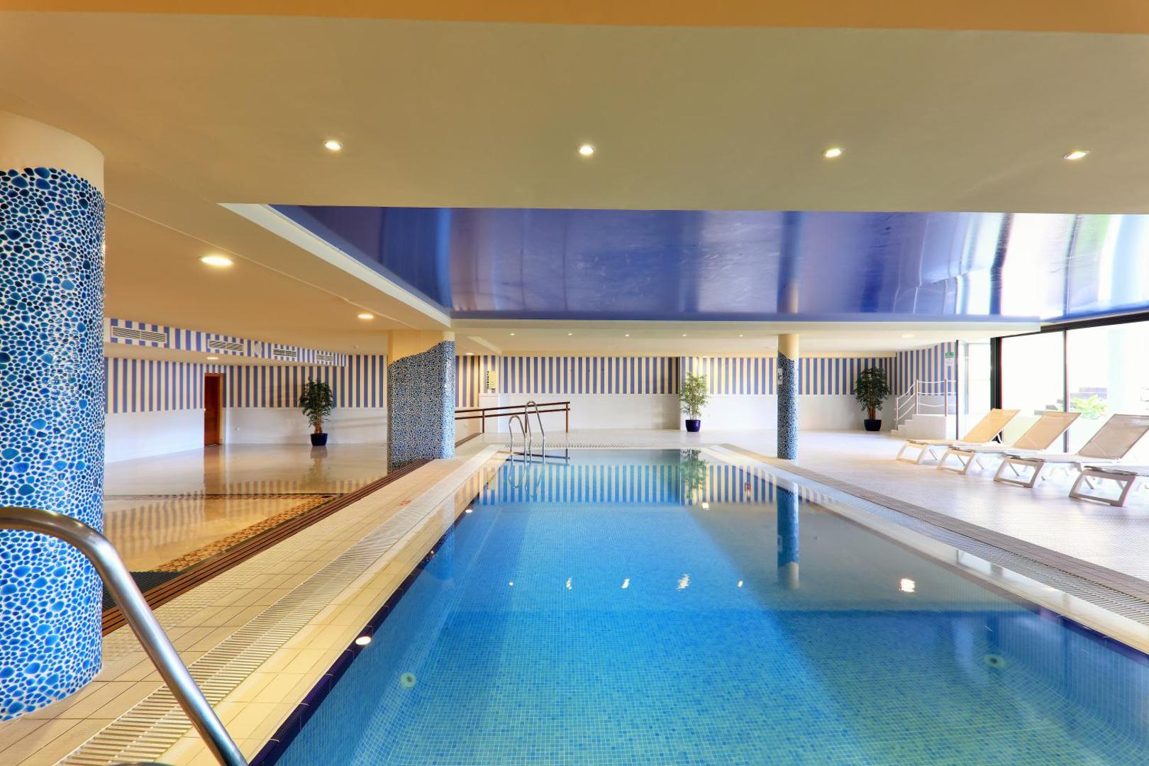 Iberostar Malaga Playa iekštelpu spa baseins ar zilu apgaismojumu un atpūtas krēsliem — moderna relaksācijas zona viesnīcas spa centrā