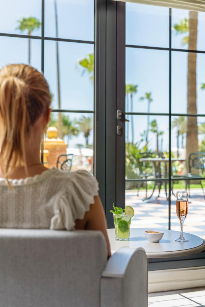 Viesis bauda atspirdzinošus kokteiļus Iberostar Malaga Playa atpūtas zonā ar skatu caur lieliem logiem uz palmu dārzu.