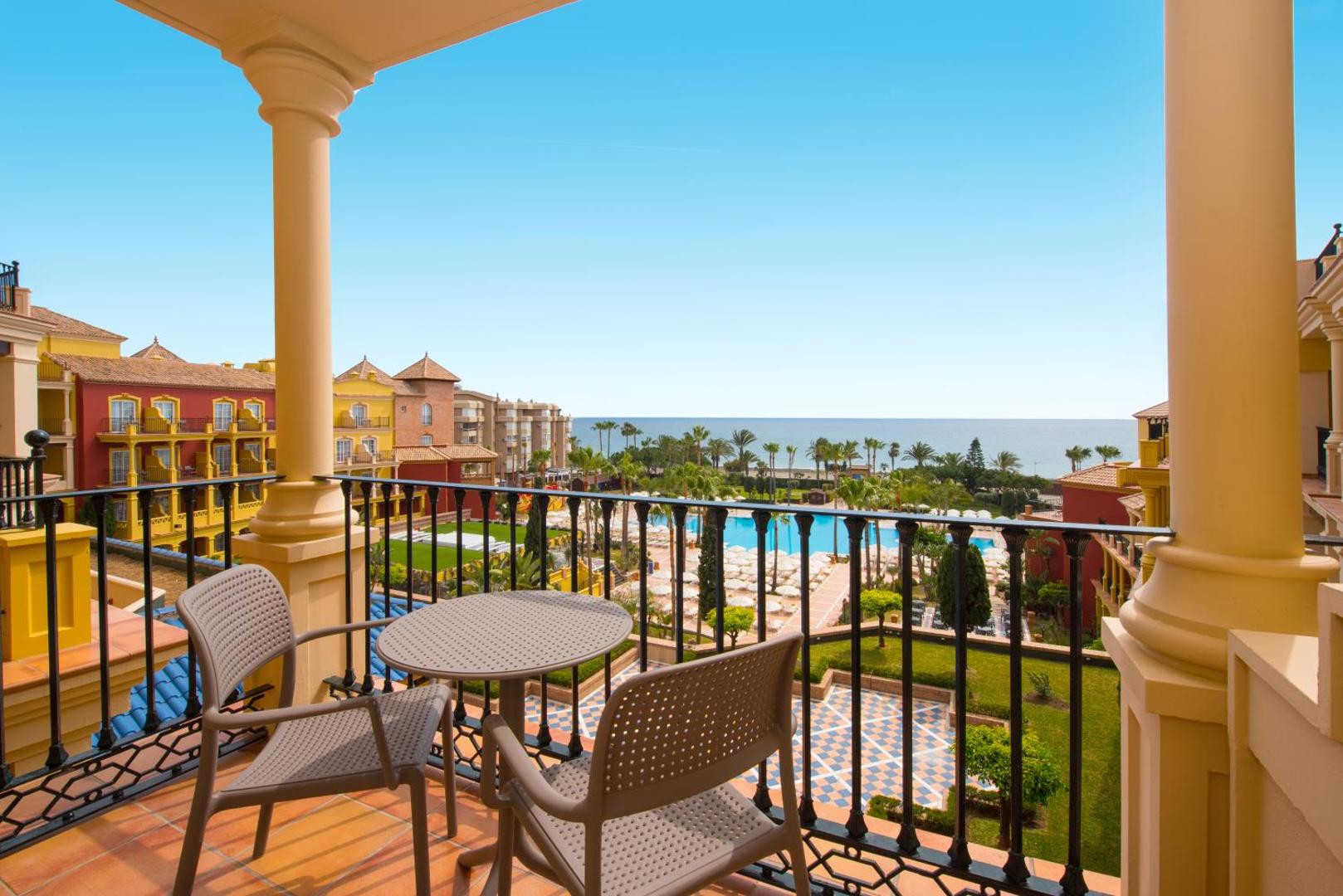 Iberostar Malaga Playa numura balkons ar galdiņu un krēsliem, skats uz viesnīcas dārzu, baseinu un Vidusjūru Andalūzijā.