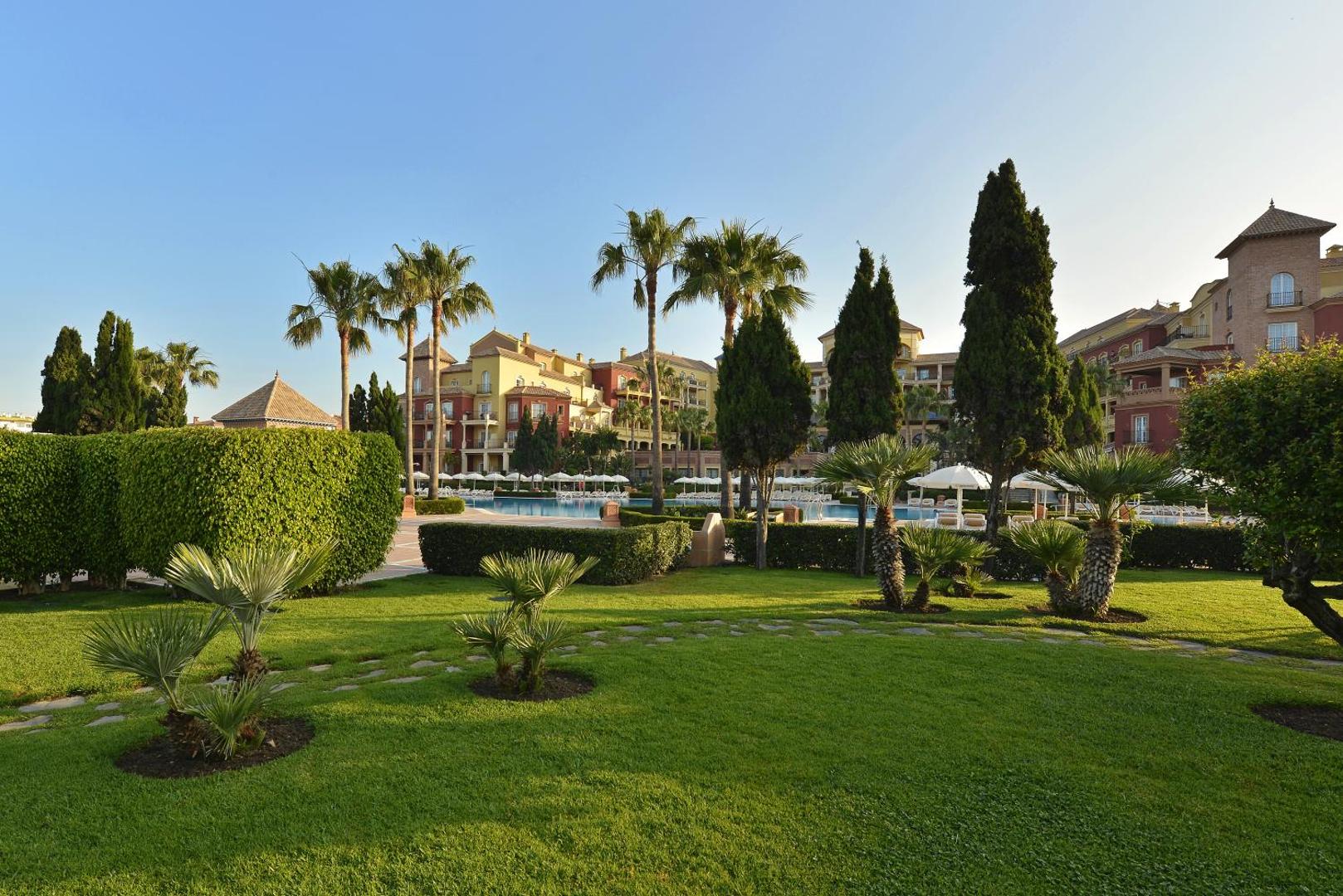 Iberostar Malaga Playa koptā dārza teritorija ar zālāju, palmām un dekoratīviem krūmiem pie baseina zonas