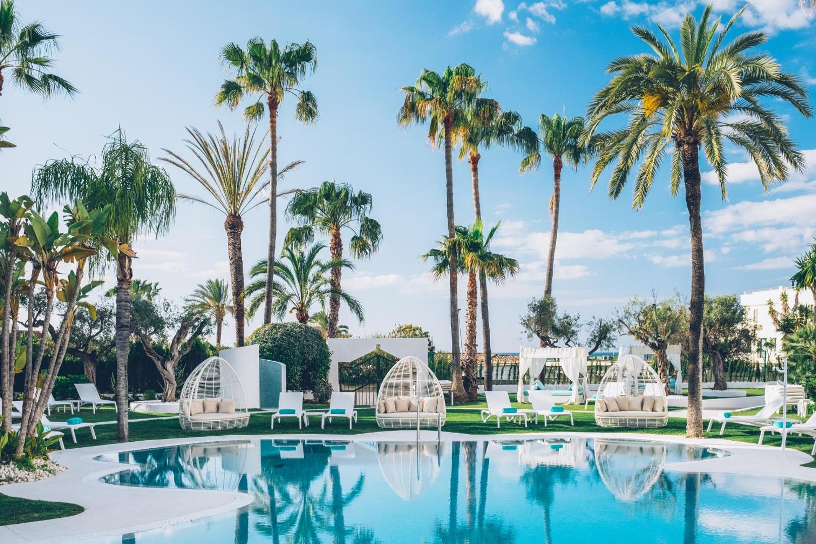 Iberostar Marbella Coral Beach āra baseins ar stilīgiem atpūtas krēsliem un palmām saulainā dienā Spānijas piekrastē