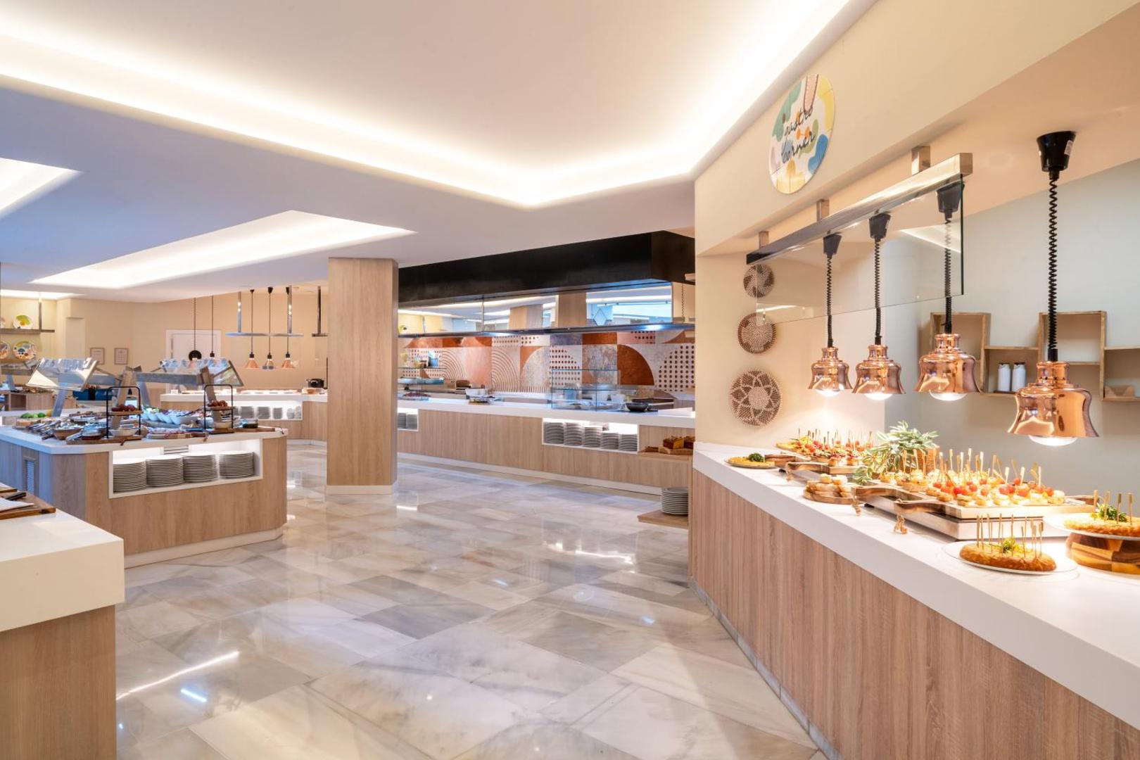 Iberostar Marbella Coral Beach bufetes tipa restorāna zona ar plašu uzkodu izvēli, modernu virtuvi un gaišu marmora grīdu.