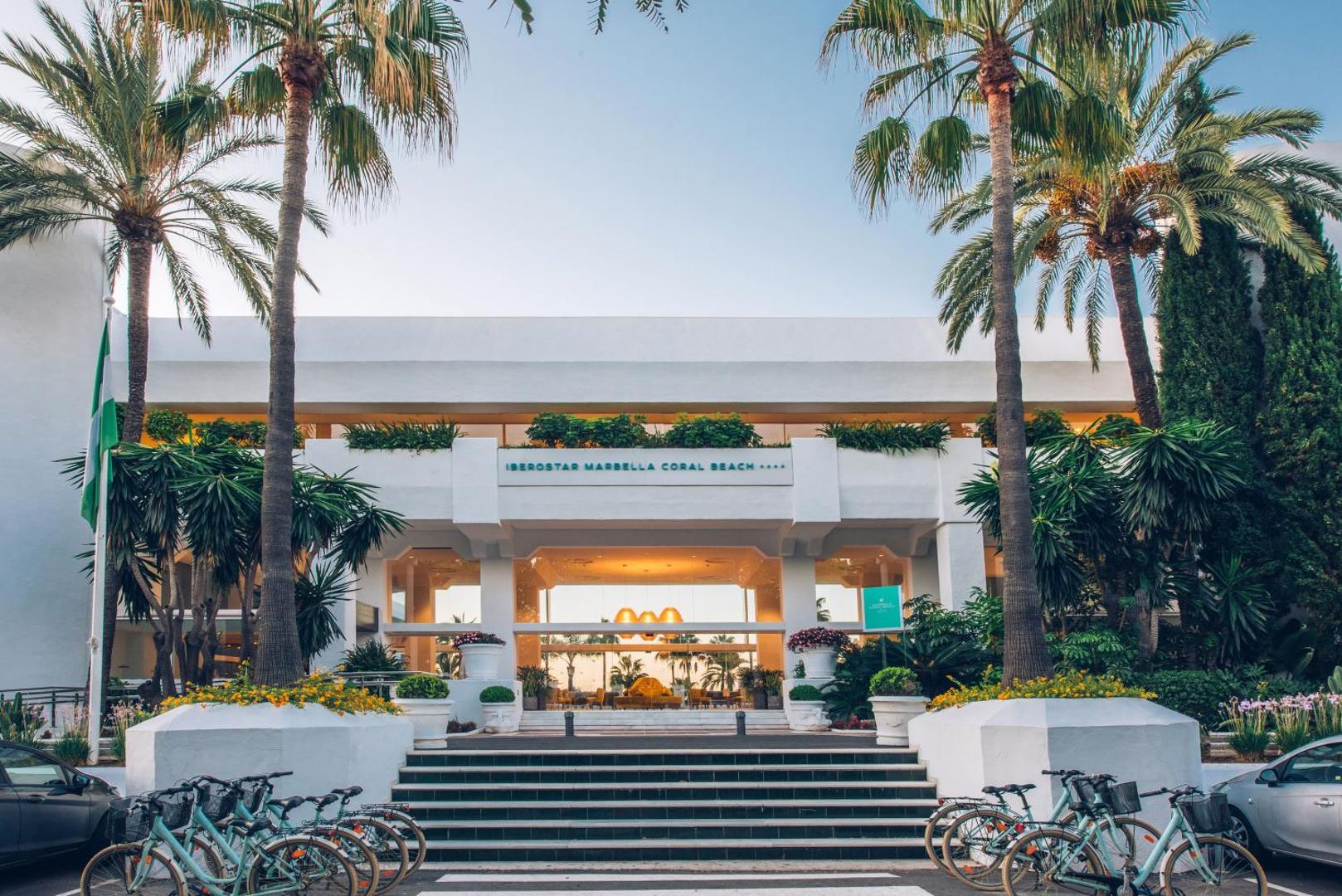 Iberostar Marbella Coral Beach galvenā ieeja ar palmām, velosipēdu nomu un modernu fasādi saulrieta gaismā