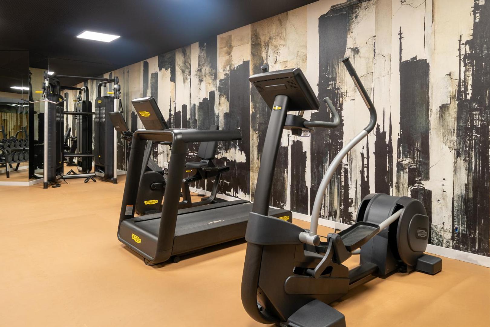 Iberostar Marbella Coral Beach trenažieru zāle ar Technogym skrejceliņiem un eliptiskajiem trenažieriem uz pilsētas silueta fona