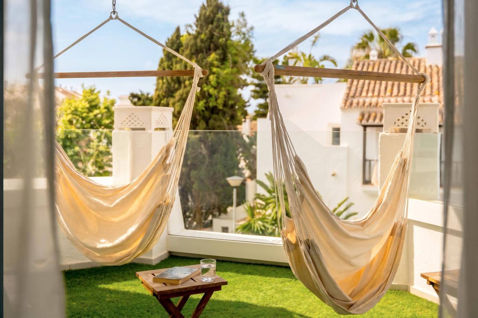 Tuvplāns Iberostar Marbella Coral Beach terasei ar diviem šūpuļtīkliem, zaļu mākslīgo zālienu un skatu uz apkārtnes balto arhitektūru un kokiem.