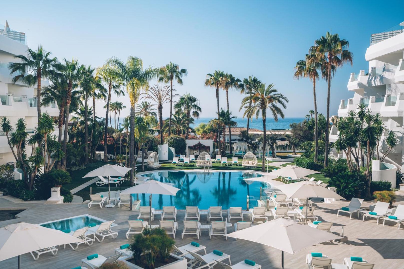 Iberostar Marbella Coral Beach viesnīcas ēka un plašā baseina teritorija ar palmām un daudziem atpūtas krēsliem no augšas