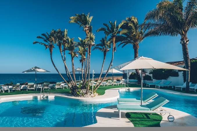 Iberostar Marbella Coral Beach baseina zona ar zviļņiem un saulessargiem tiešā jūras tuvumā zem skaidrām debesīm