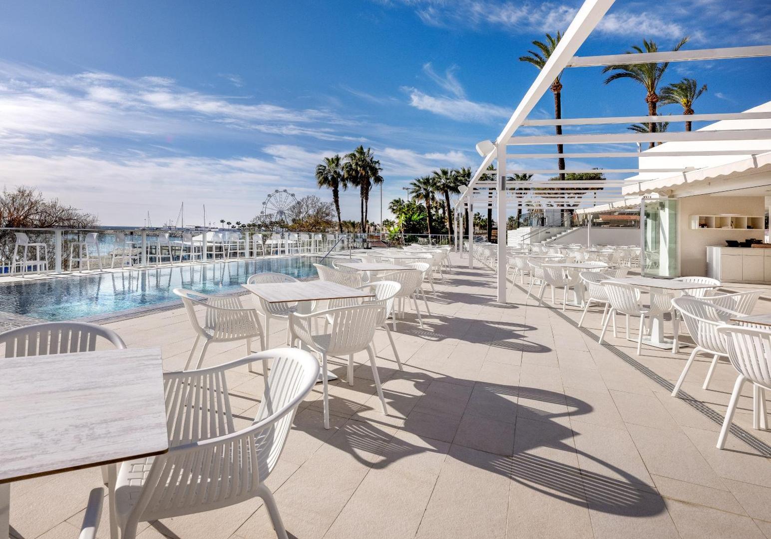 Ocean House Costa del Sol plašā āra terase ar baltiem galdiem un krēsliem blakus baseinam piekrastē