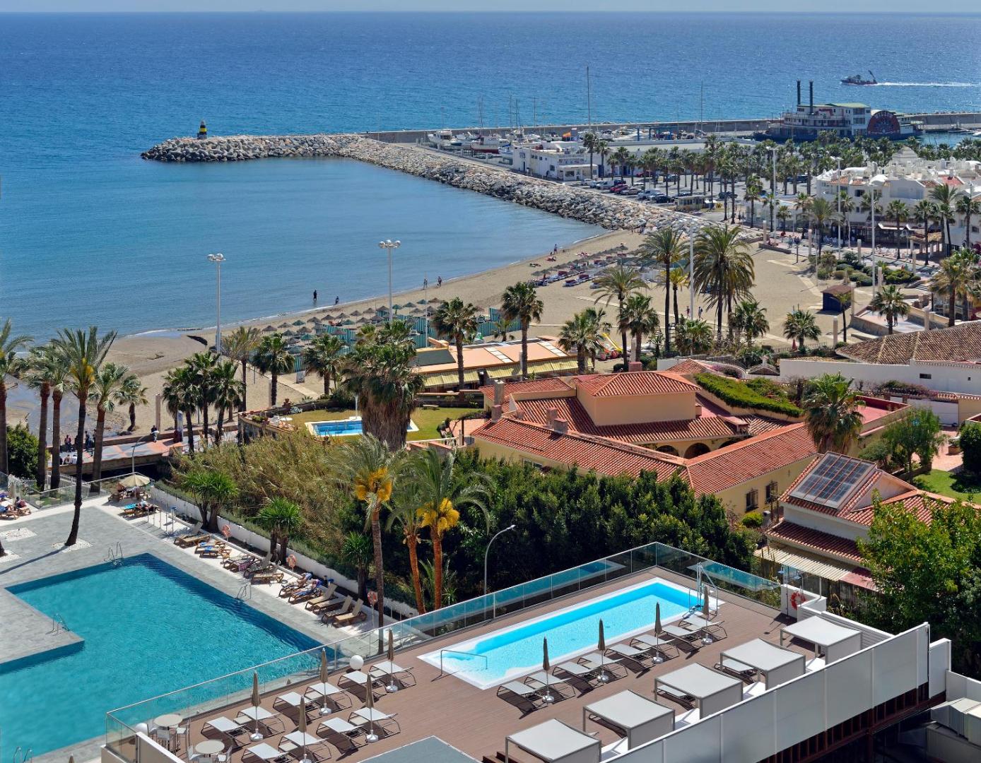 Skats no Ocean House Costa del Sol terases uz baseinu, pludmali un jahtu piestātni — atpūtas zona ar sauļošanās krēsliem