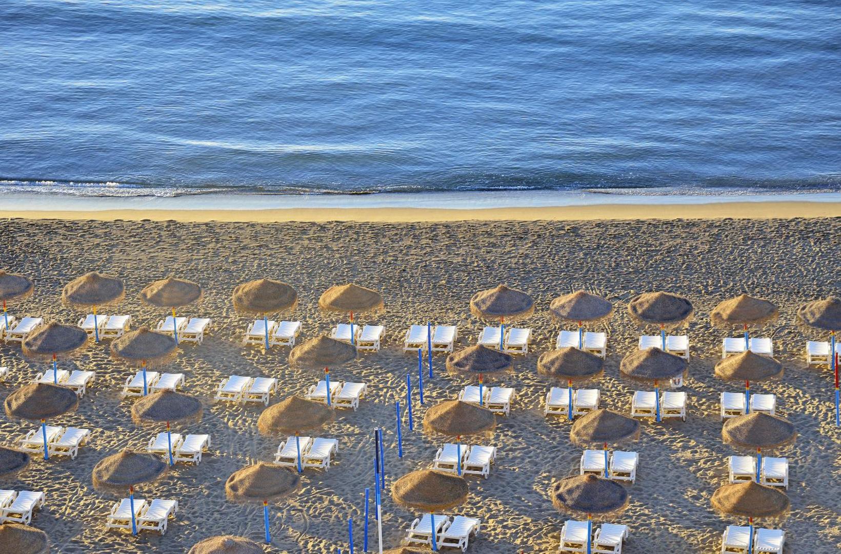 Skats no augšas uz Ocean House Costa del Sol smilšu pludmali ar saulessargiem un zviļņiem pie jūras