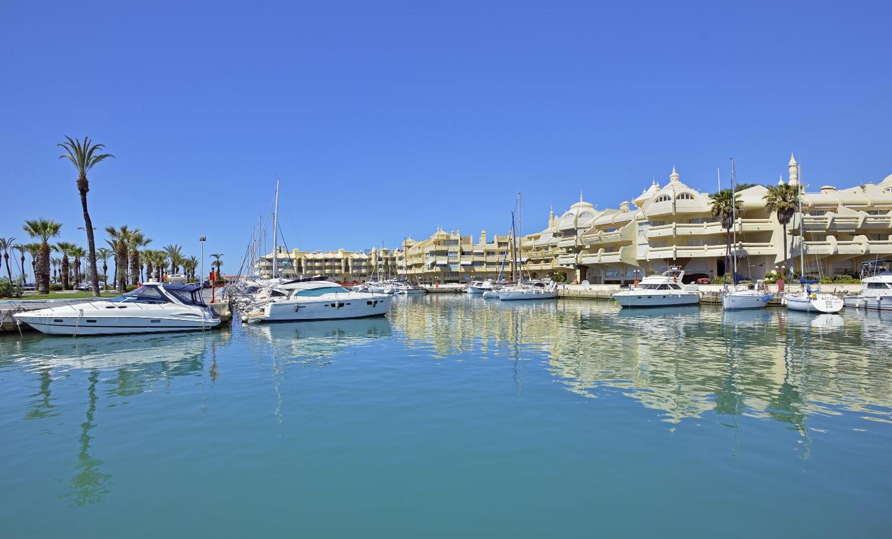 Skats uz Ocean House Costa del Sol arhitektūru un jahtu piestātni no ūdens puses zilās debess fonā