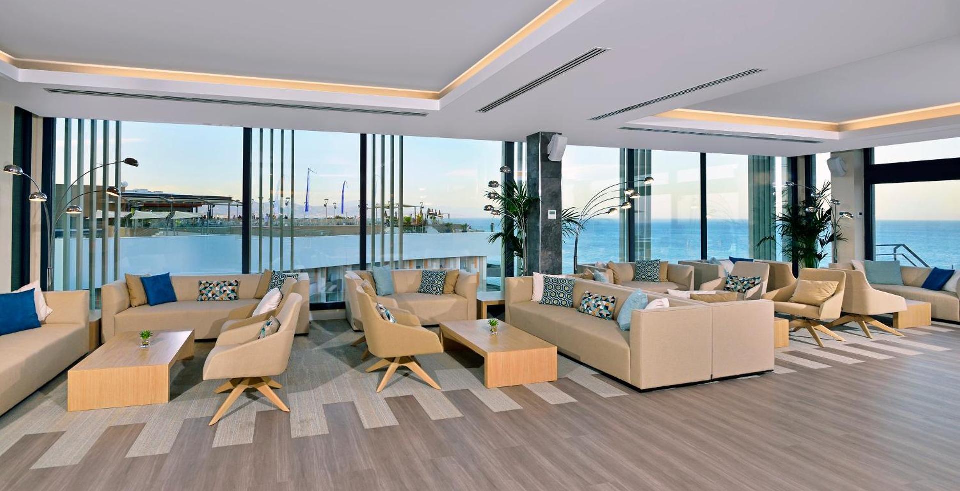 Melia Costa del Sol plašā lobby atpūtas zona ar mīkstajiem dīvāniem un panorāmas logiem uz jūru saulrietā