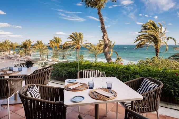 Gran Melia Don Pepe restorāna terase ar skatu uz jūru — eleganti klāti galdi, pīti krēsli un palmas piekrastē