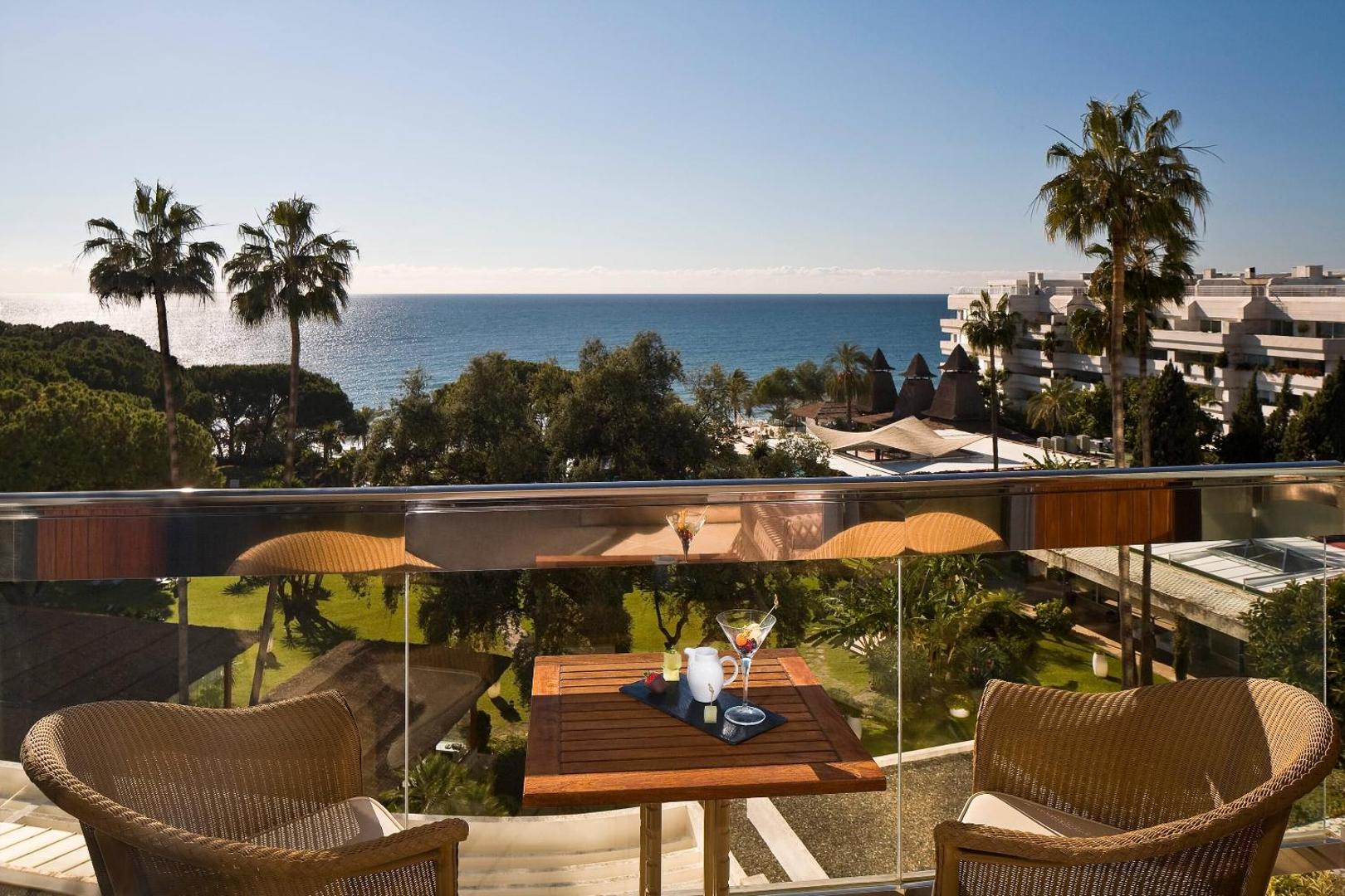 Gran Melia Don Pepe viesnīcas terase ar skatu uz dārzu un jūru — saulains laiks, palmas un dzērieni uz galda