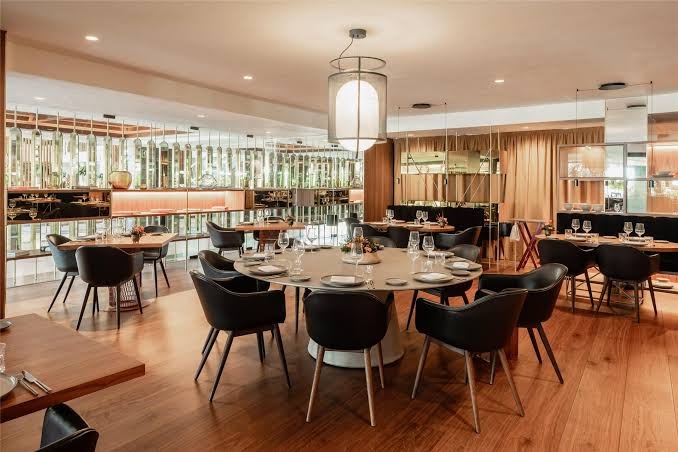 Gran Melia Don Pepe restorāns ar modernu dizainu, apaļiem galdiem, melniem krēsliem un dizaina apgaismojumu siltos toņos