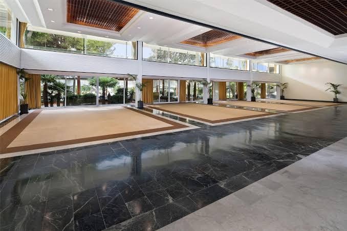 Gran Melia Don Pepe viesnīcas plašā lobby zona ar marmora grīdām, augstiem griestiem un skatu uz dārzu caur lieliem logiem