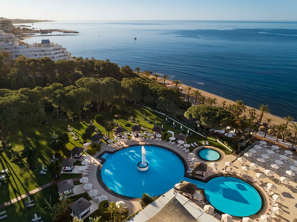 Gran Melia Don Pepe viesnīcas skats no augšas uz baseinu kompleksu un pludmali Marbeljā — plaša zaļā zona ar palmām un Vidusjūras piekrasti