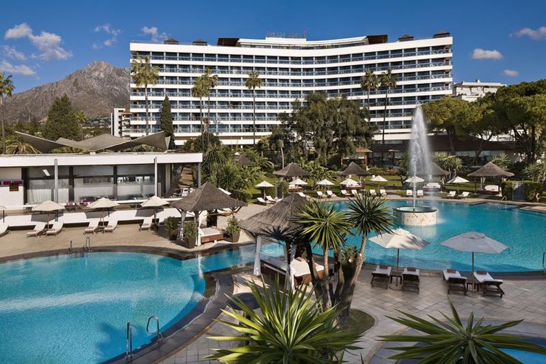 Gran Melia Don Pepe viesnīcas galvenā ēka un āra baseins ar strūklaku Marbeljā — fonā redzami kalni un labiekārtota atpūtas zona
