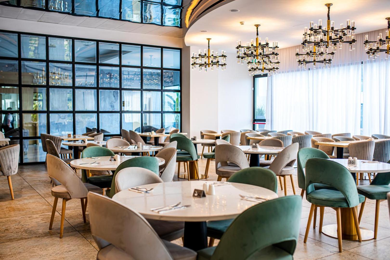 At Herbal Boutique Hotel & Spa modernais restorāns ar dizaina lustrām, lieliem logiem un elegantiem krēsliem gaišos un zaļos toņos.