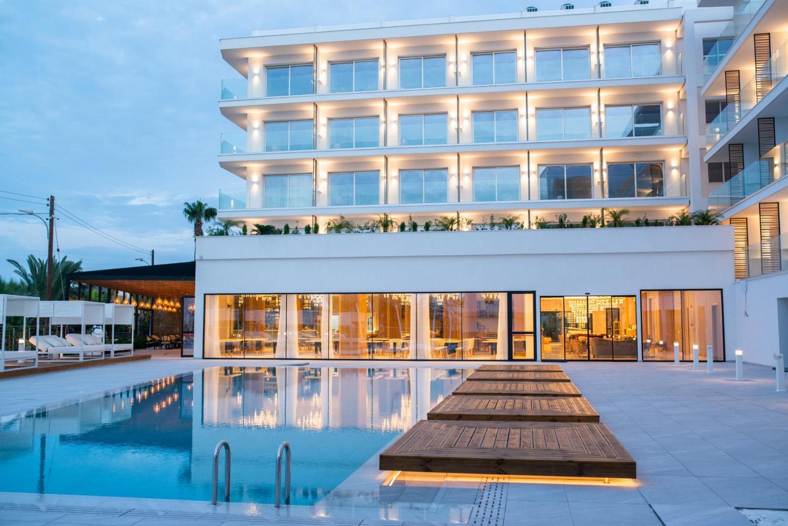 At Herbal Boutique Hotel & Spa āra baseins vakarā ar koka terasi un viesnīcas ēkas atspulgu ūdenī Protarasā