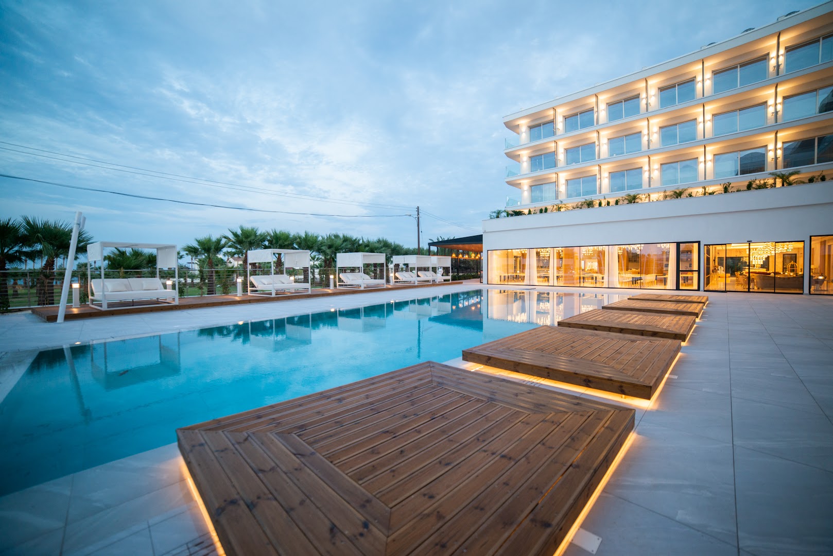At Herbal Boutique Hotel & Spa modernā fasāde un izgaismots baseins vakarā ar koka atpūtas platformām un stilīgiem bungalo tipa krēsliem