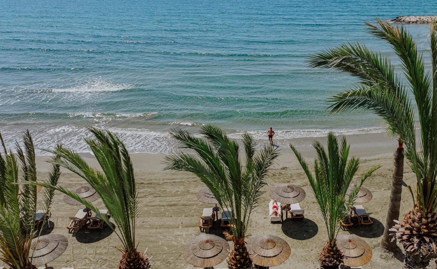 Skats no augšas uz Golden Bay Beach pludmali ar palmām, salmu saulessargiem un zilo Vidusjūras piekrasti Larnakā.