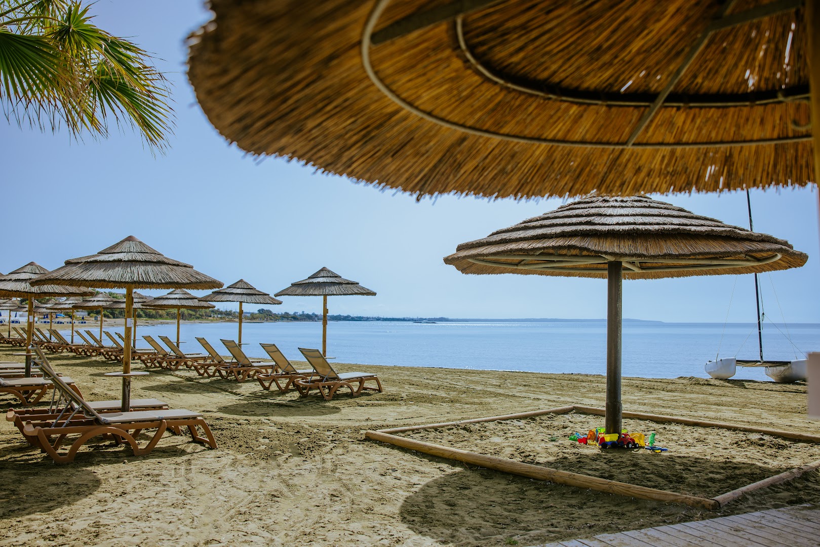 Golden Bay Beach smilšu pludmale ar salmu saulessargiem, sauļošanās krēsliem un bērnu rotaļu stūrīti smiltīs pie jūras.