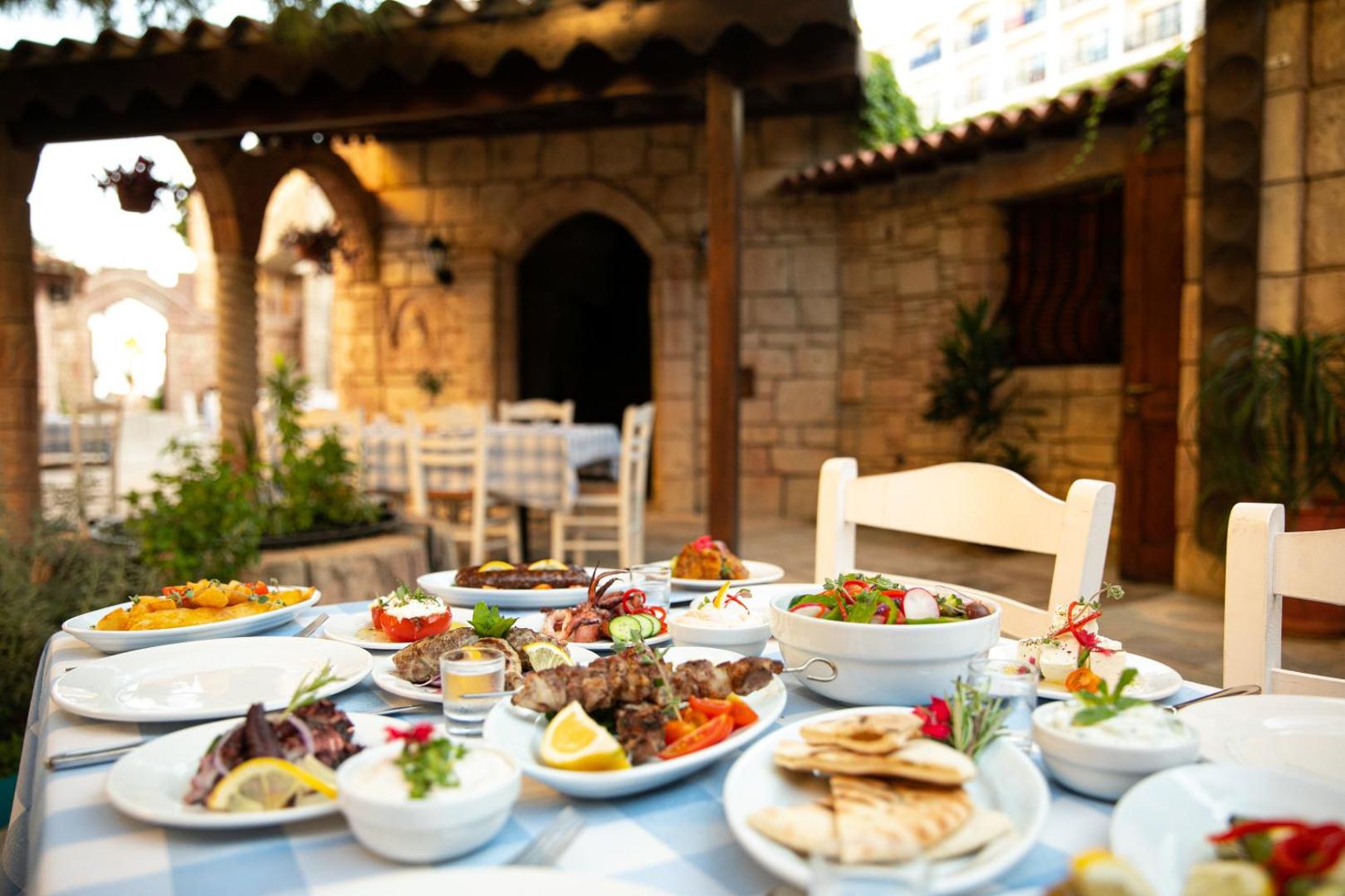 Tradicionāls grieķu virtuves galds ar uzkodām un grilētu gaļu Golden Bay Beach restorāna āra terasē
