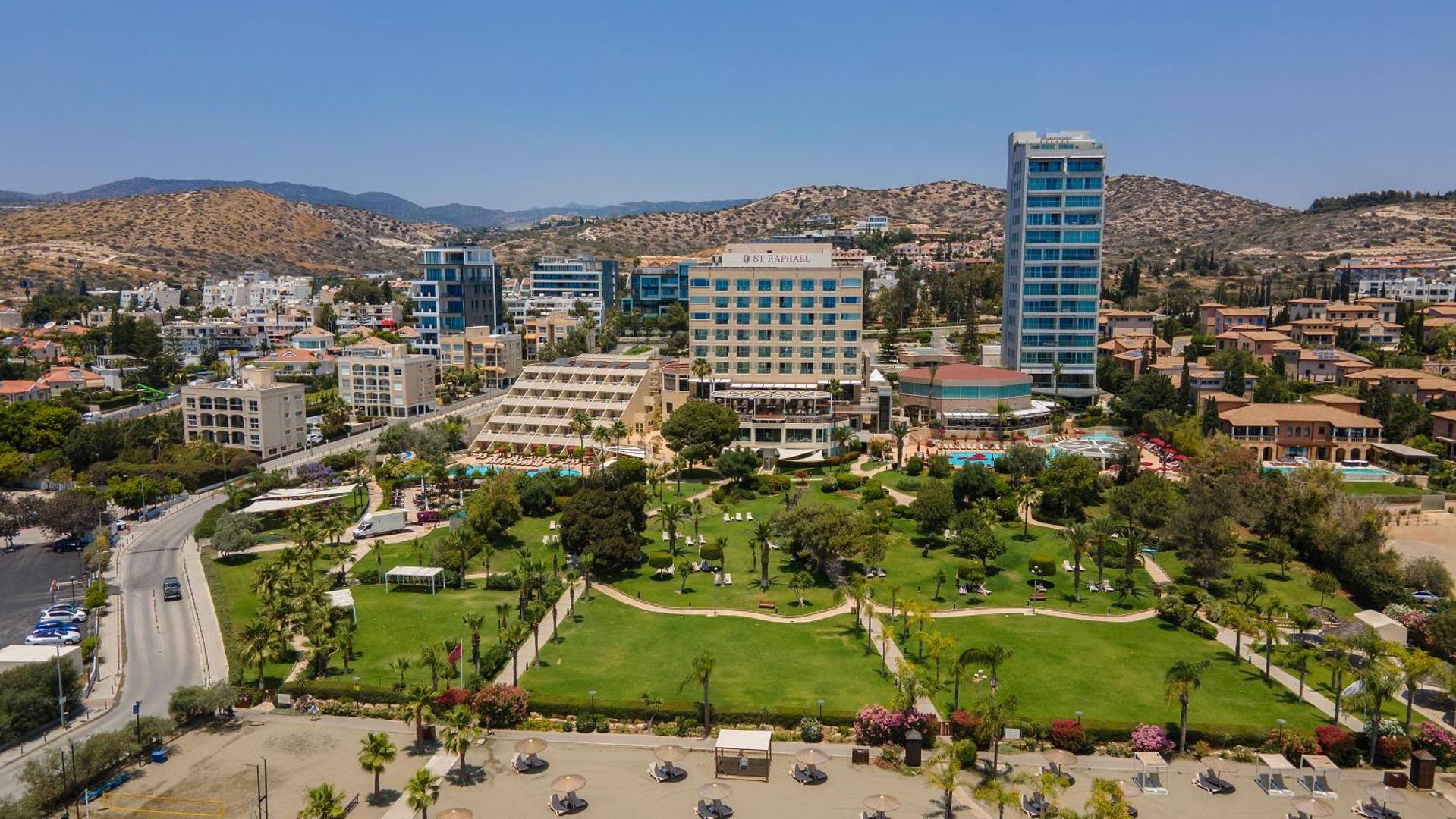 St. Raphael Resort panorāmas skats no augšas Limasolā — plaša zaļā zona, baseini un viesnīcas komplekss piekrastes joslā