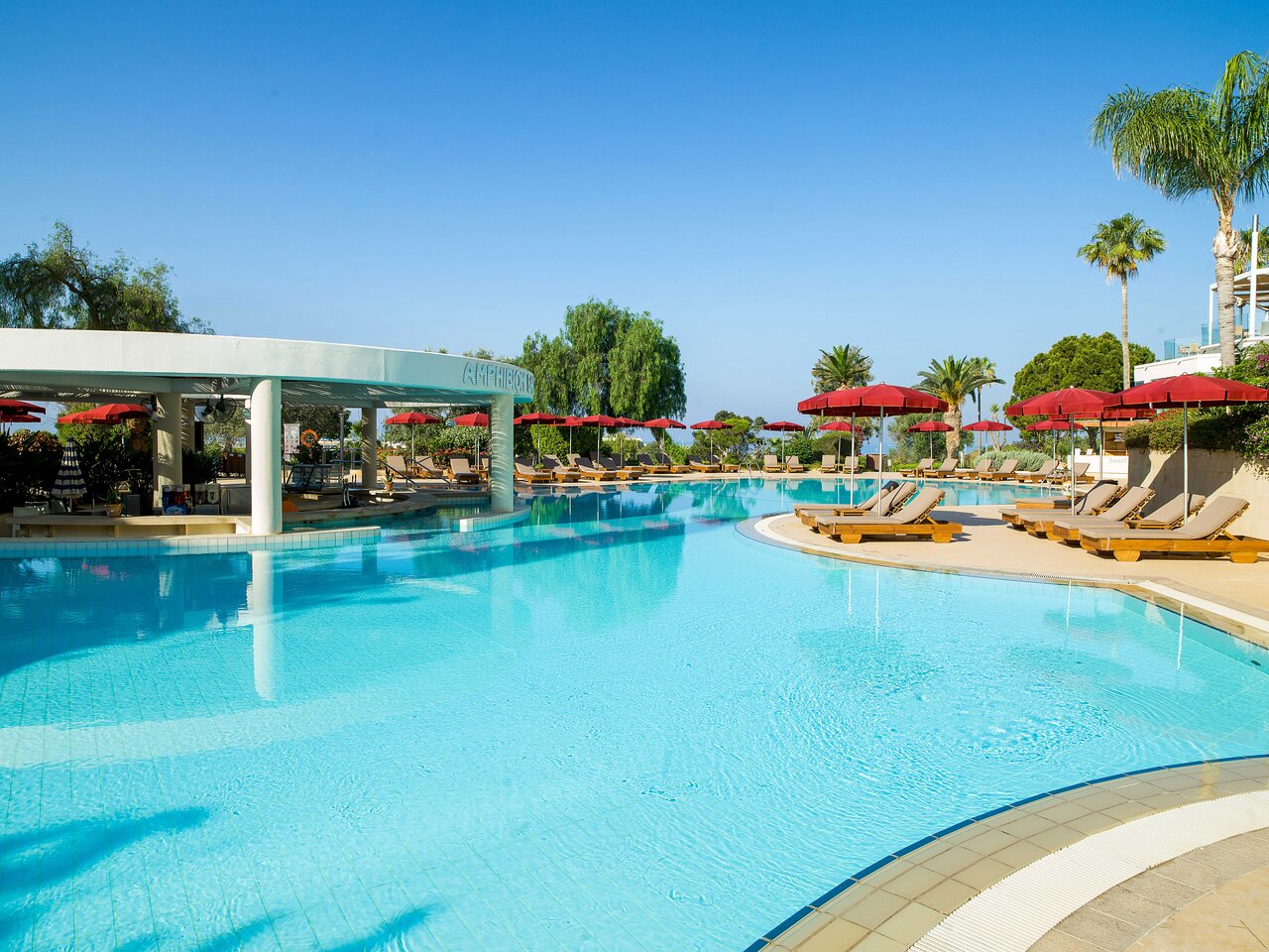 Plašs St. Raphael Resort āra baseins ar bāru ūdenī un daudziem sauļošanās krēsliem saulainā dienā Limasolā, Kiprā