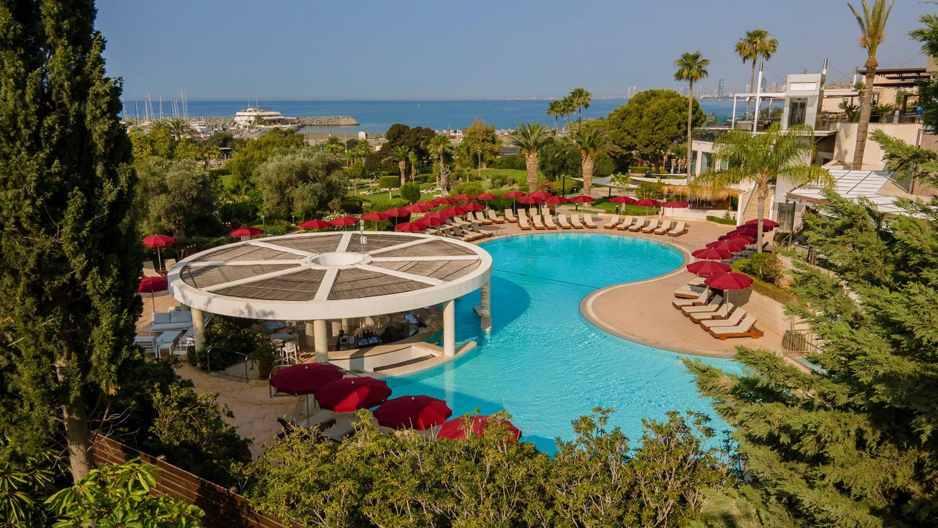 St. Raphael Resort āra baseins ar bāru zem jumta, sarkanajiem saulessargiem un skatu uz jūru Limasolā