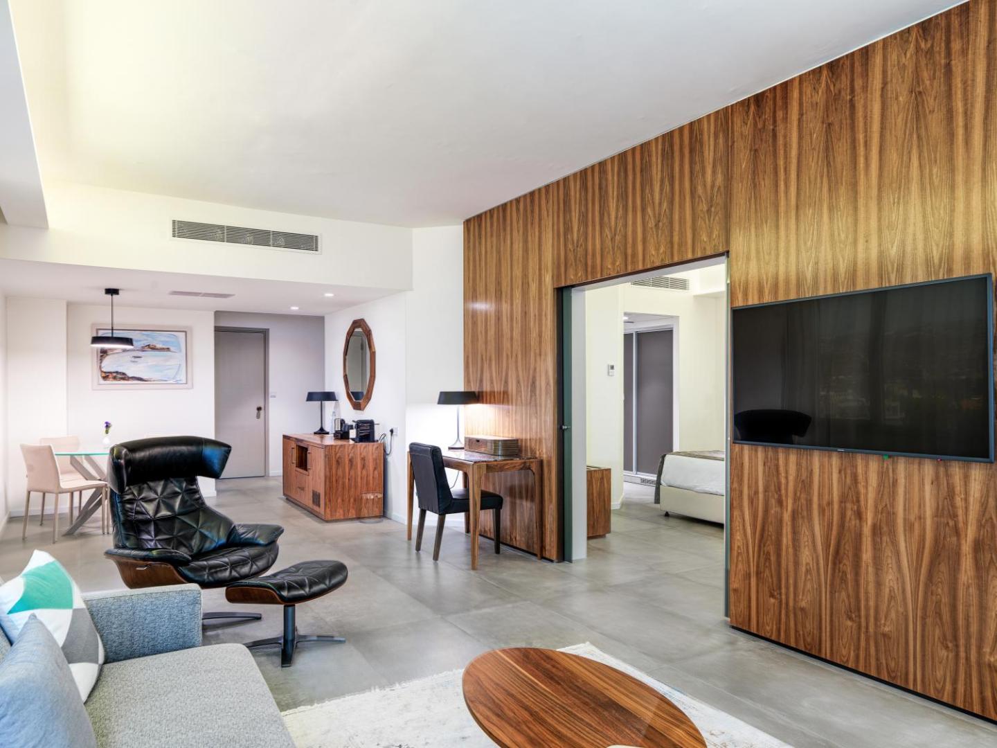 St. Raphael Resort plašs viesistabas numurs ar modernām mēbelēm un koka apdari — atpūtas zona ar TV un dizaina krēslu