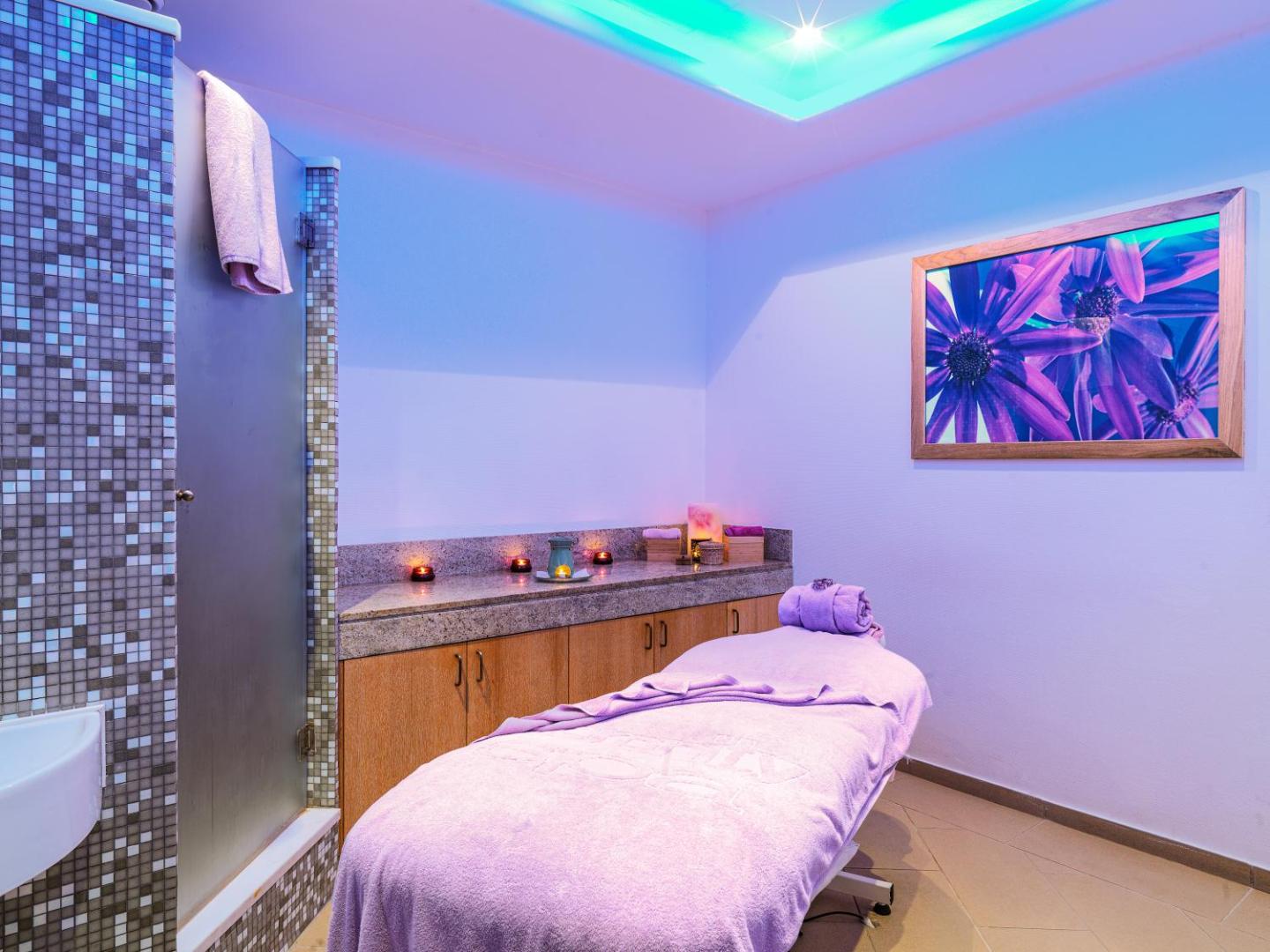 St. Raphael Resort spa procedūru telpa ar masāžas galdu, violetu apgaismojumu un mierīgu atmosfēru — relaksācijas zona viesnīcā