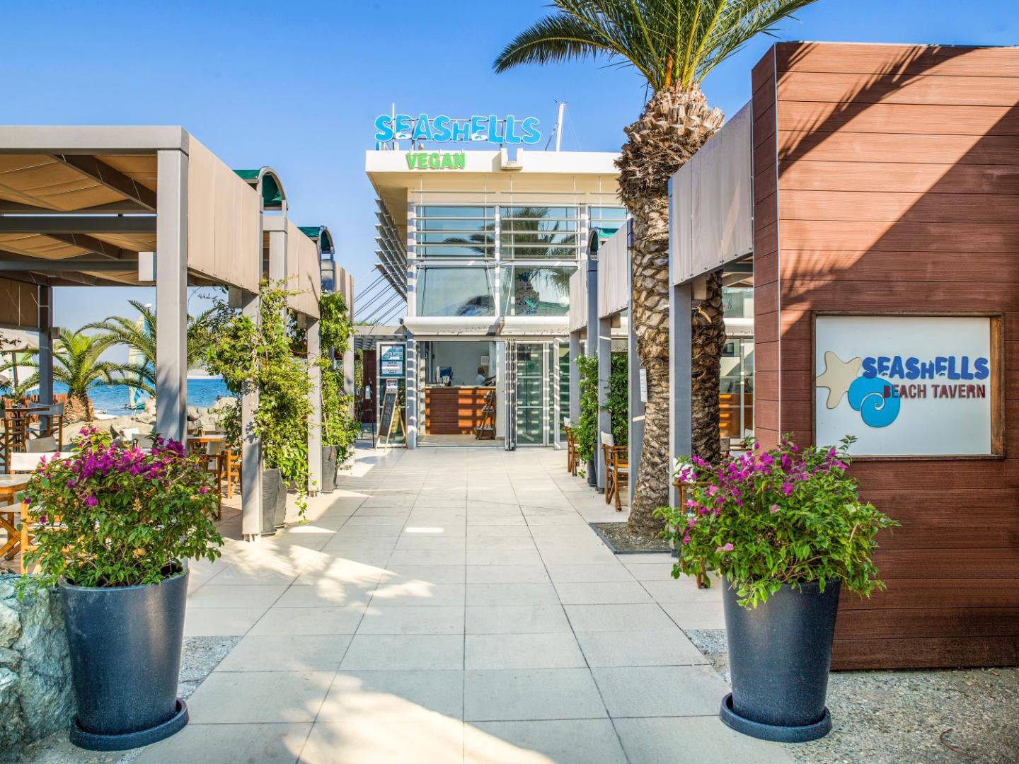 St. Raphael Resort pludmales restorāns Seashells Vegan Tavern ar modernu ieeju, palmām un ziedu dekoriem piekrastē