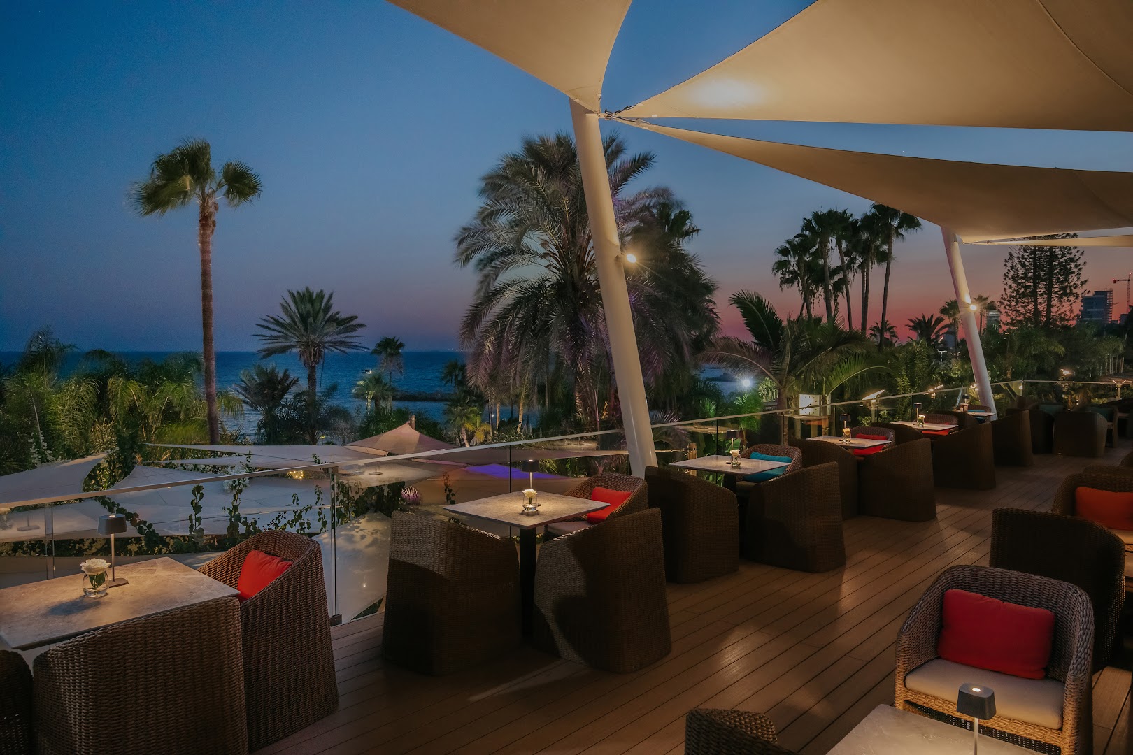 Amathus Beach āra terases restorāns vakarā ar skatu uz Vidusjūru un palmām saulrieta laikā Limasolā, Kiprā